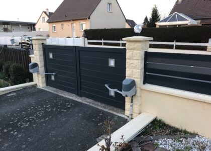 Portail battant gris motorisé entre des piliers en pierre.