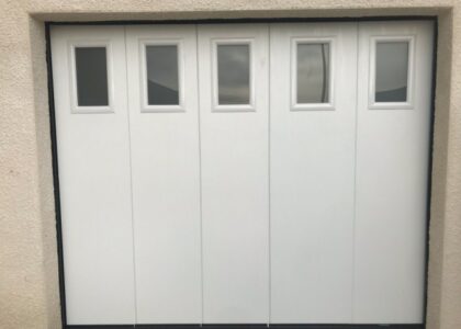 Porte de garage sectionnelle blanche avec petits hublots.